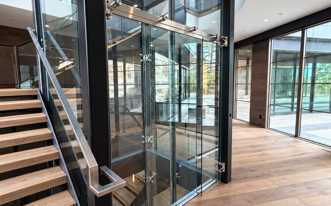 Custom glass elevator with black steel shaft beside an oak staircase in a modern luxury residence
