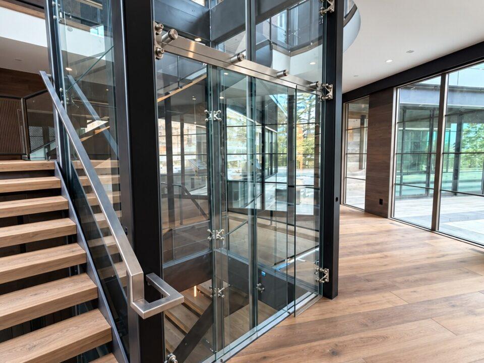 Custom glass elevator with black steel shaft beside an oak staircase in a modern luxury residence